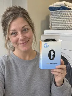 A wife in a grey sweatshirt by the laundry, holding up the open box with the band inside.