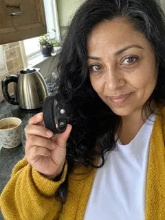 A wife in a yellow cardigan in her kitchen, a cup of chai beside her, holding up the band.