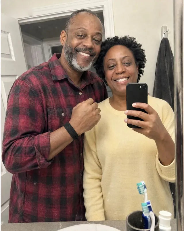 Denise and Curtis smiling in their bathroom mirror, the band on his wrist.