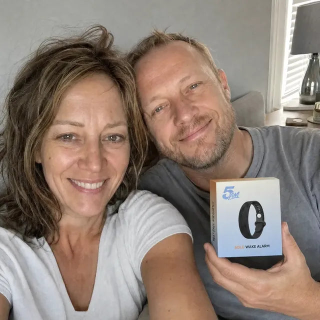 A couple cheek to cheek in bed, holding up the Solo Wake Alarm box.