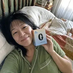 She smiles from her pillow in morning light, holding the Solo Wake Alarm box.