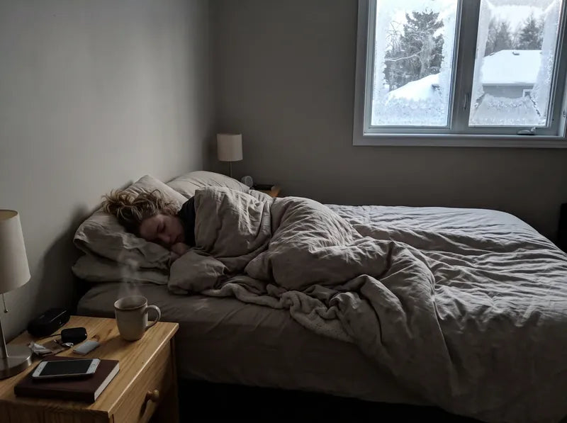 6:30 AM: she sleeps on in soft winter light, a coffee waiting on her nightstand, his side of the bed empty.