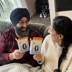 A couple on the sofa under a blanket, smiling at each other, each holding an open box.