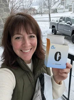A wife in a green vest on a snowy porch, holding the open box.